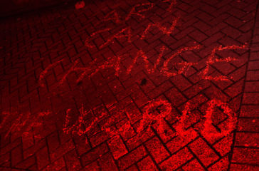 Written in chalk on the pavement, it reads 'Art Can Change The World' the photo has a red wash.