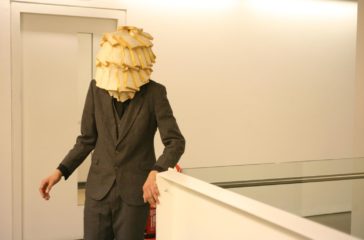 A man in a suit stands at the top of a white staircase, his face is covered in white bread.