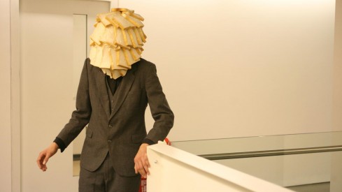 A man in a suit stands at the top of a white staircase, his face is covered in white bread.