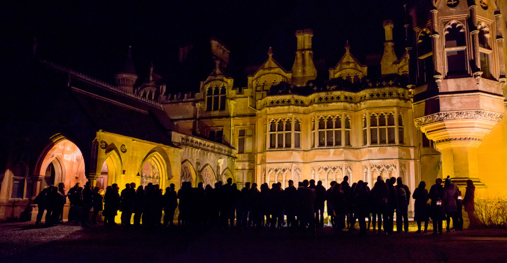 A crowd of people are silhouetted outside Tyntesfield Manor.