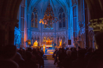 Patrick Wolf is on stage in Tyntesfield Chapel, he is standing in front of a keyboard. There are other instruments around him. The audience are sat watching Night Songs.