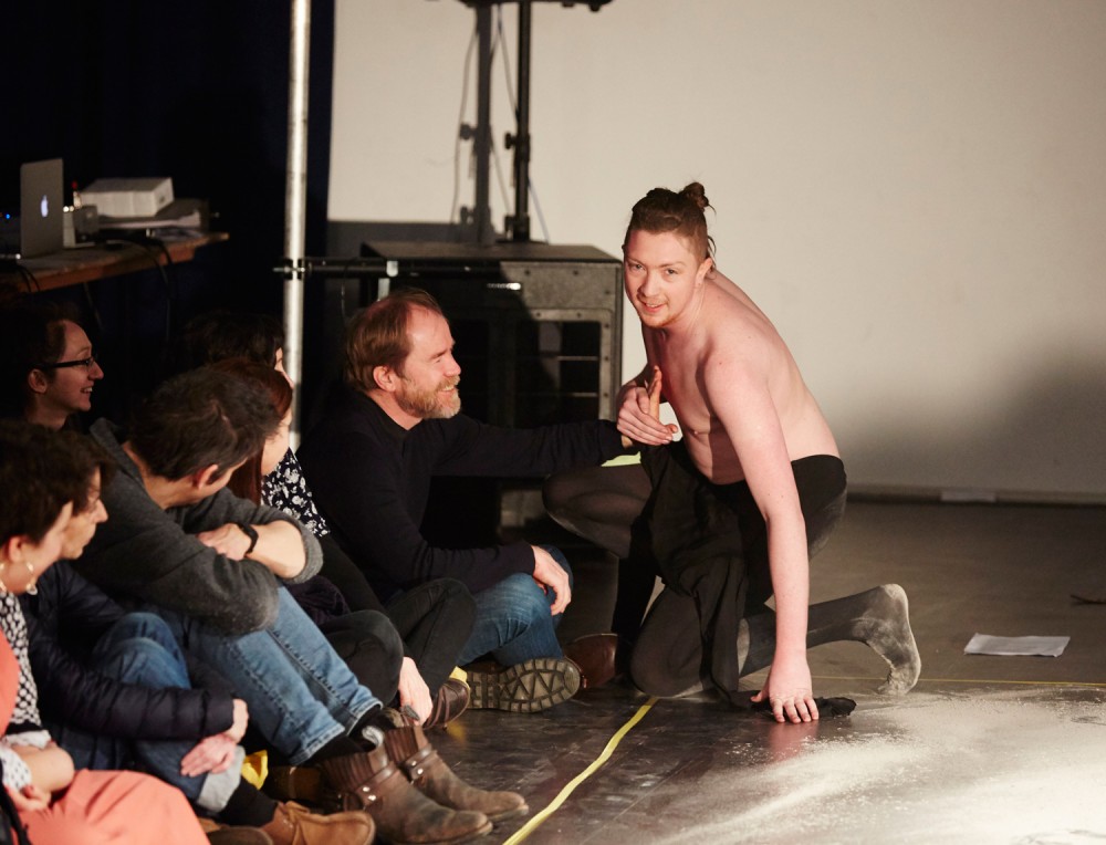 One of the performers in bent down and is holding an audience members hand against his chest.