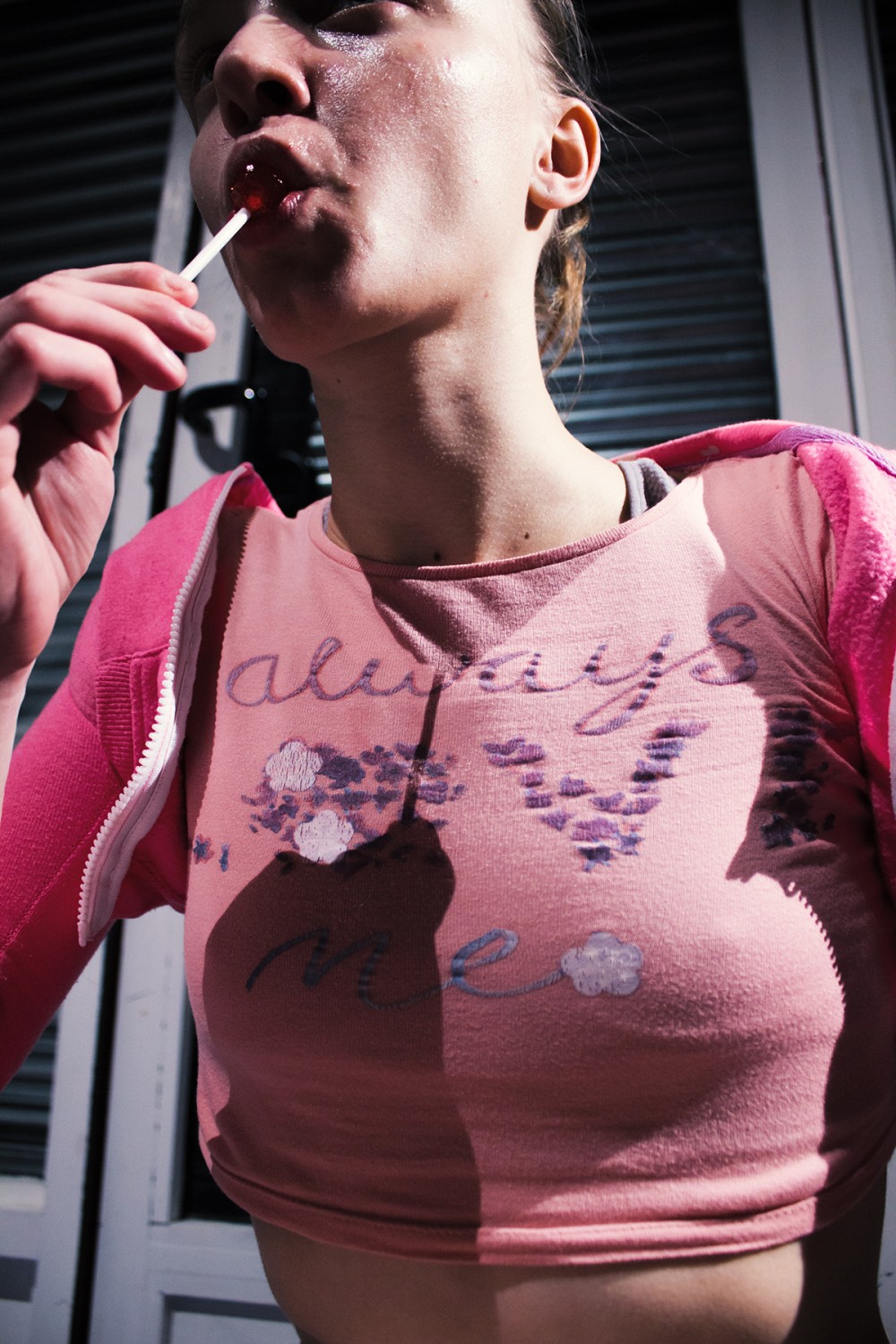 A woman wearing a tank top is sucking a lollipop.