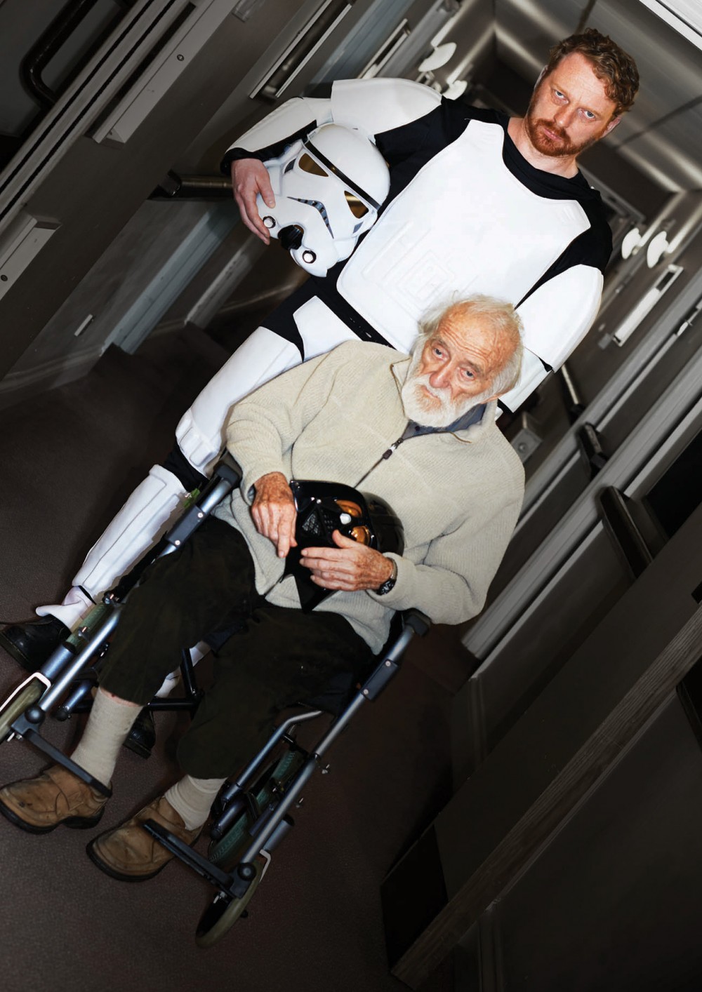 Kim Noble is dressed as a Storm Trooper, he is pushing an old man in a wheel chair towards the us.