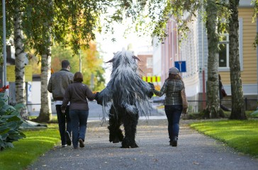 Beastie walks down a path, holding hands with a group of people.