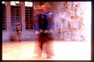 A blurred image of two people dressed as cowboys in an empty warehouse.