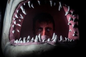 A man painted red is inside a sharks head.