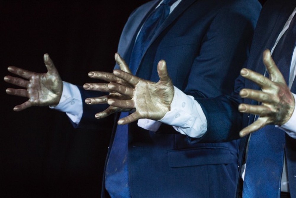 A close up of two sets of hands, painted in gold.