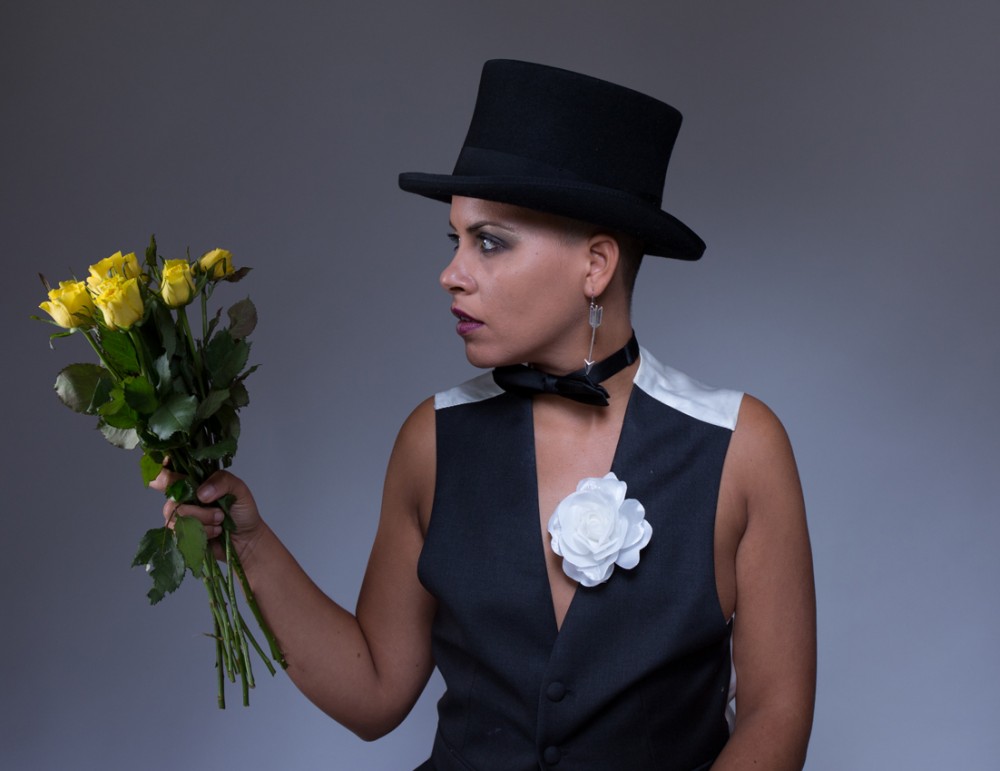 Ria is dressed in a black and white waist coat and a top hat, she is holding a bunch of flowers.