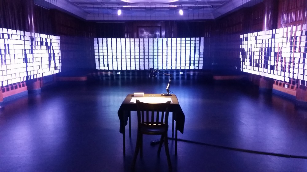 A table and chair are centred in a empty blue room.