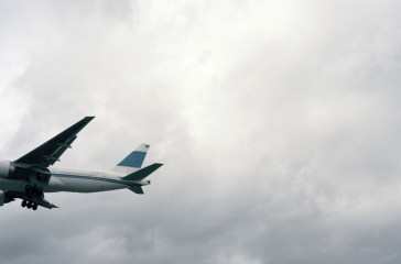 A commercial plane flies across a bright white sky.