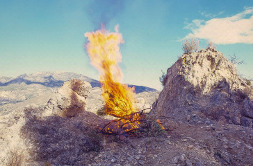 A rocky surface in the middle of the desert, a fire blazes in the centre.