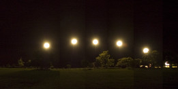 Five flood lights light up a green field at night.
