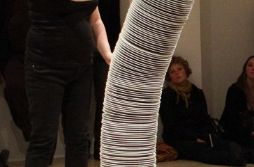 A woman stands facing a six foot stack of plates.
