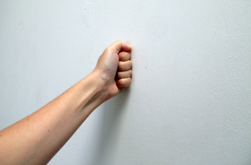 A fist is pressed up against a white wall.