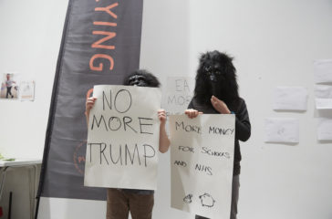 Two children are wearing gorilla masks and are holding signs that read 'no more trump' and 'more money for schools and nhs'