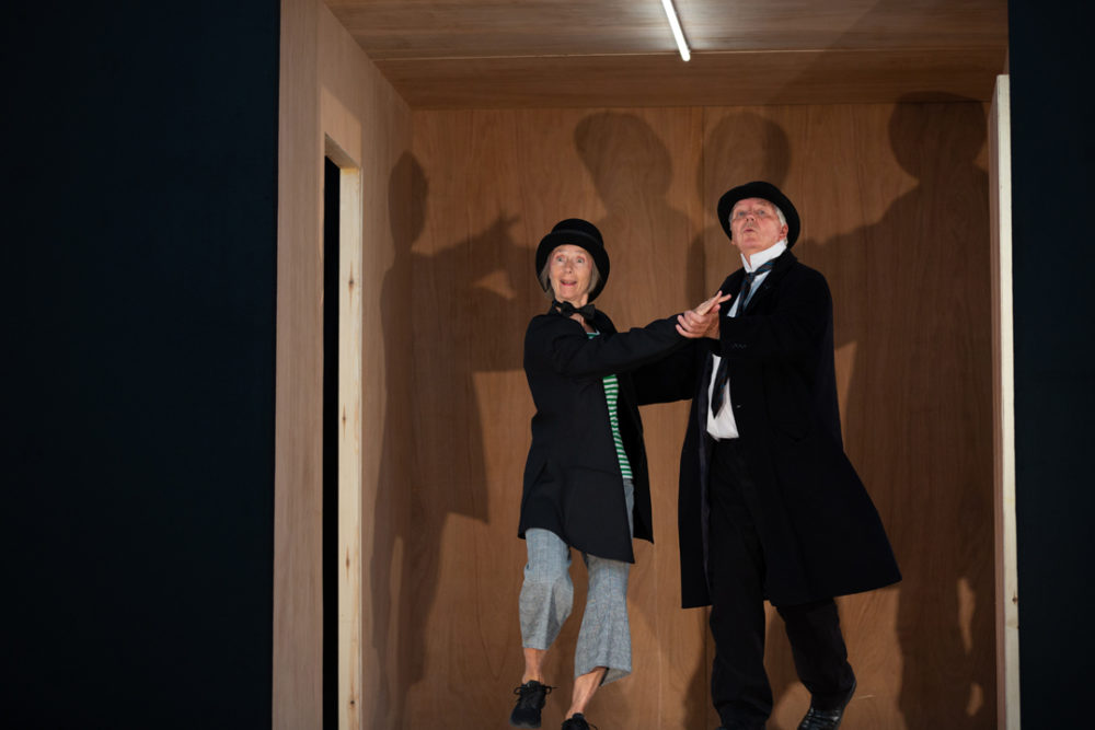 A man and a woman dressed in bowler hats and smart black jackets dancing.