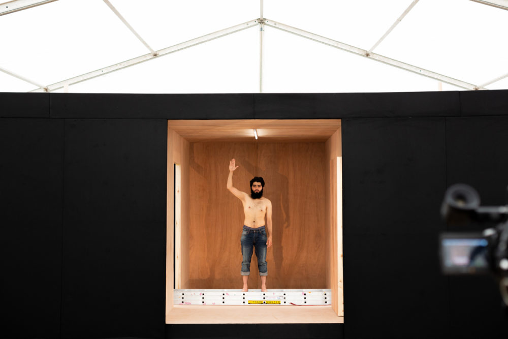 Topless man waves from small room