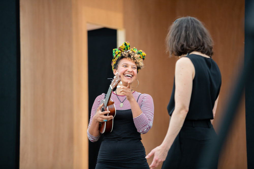 A woman with holds a ukulele and laughs