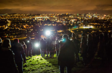 A photo from NIghtwalks with teenagers. An audience look over Bristol from a hill at nighttime.