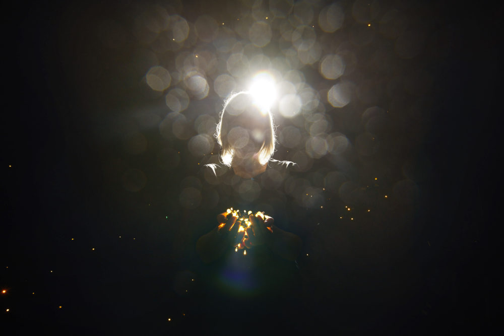 A woman stands in a dark space holding up a collection of lights to the camera