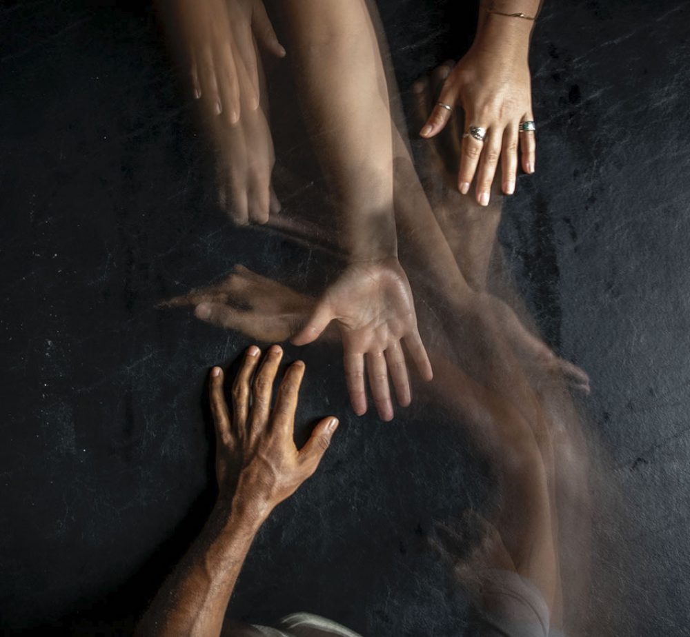 A timelapse photo of hands reaching out to each other across a black background